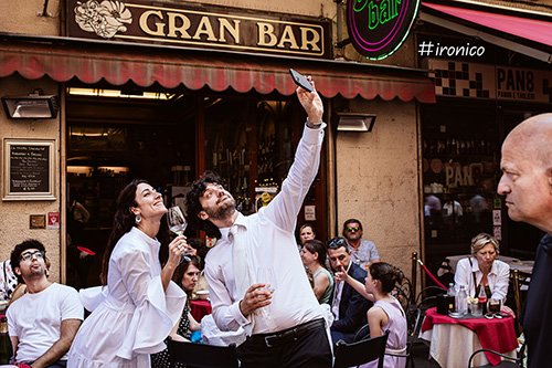 foto con sposi che fanno un selfie mentre un passante li guarda